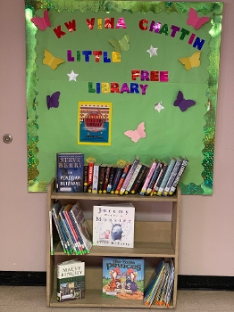 small bookshelf with children's books under green bulletin board wall sign reading 